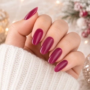 May include: A hand with manicured nails painted in a glossy, deep magenta-pink shade. The nails are shaped in a rounded oval style, featuring a smooth, reflective finish that highlights the vibrant, saturated color of the nail polish.