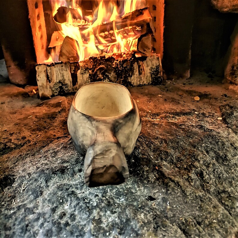 May include: A wooden bowl with a natural finish sits in front of a fireplace. The bowl is empty and has a rounded shape with a handle.