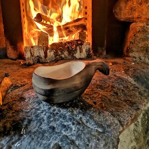 May include: A dark brown wooden bowl with a white interior, sitting on a rough, textured surface near a fireplace.