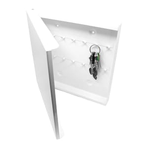 Peut inclure: Un porte-clés blanc avec une porte à charnière, comportant plusieurs crochets pour les clés. La porte est légèrement entrouverte, révélant un jeu de clés suspendues à un anneau. Le porte-clés a un design minimaliste.