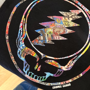 May include: Black t-shirt with a vibrant skull and lightning bolt graphic. The design includes a collage of images and the text "COSMIC CHAOS". The skull and lightning bolt are outlined in white.