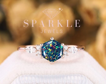 Könnte beinhalten: Ein Ring aus Roségold mit einem sechseckigen schwarzen Opal-Edelstein, umgeben von kleineren weißen Diamanten. Der Ring liegt auf einem weißen Samtkästchen. Auf dem Kästchen steht SPARKLE JEWELS.