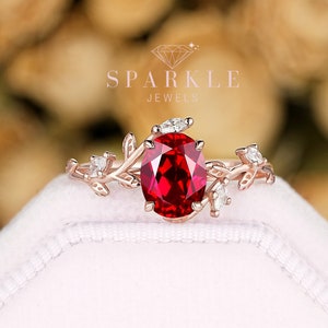 May include: A rose gold engagement ring with a large oval ruby gemstone surrounded by smaller diamonds. The ring features a delicate floral design with leaves and branches.