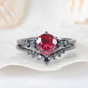 May include: A black gold engagement ring set with a large red gemstone surrounded by smaller black gemstones.