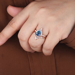 K&ouml;nnte beinhalten: Ein Verlobungsring mit einem birnenf&ouml;rmigen blauen Edelstein, einem zarten V-f&ouml;rmigen Band und kleineren wei&szlig;en Edelsteinen. Der Ring ist in Ros&eacute;gold gefasst.