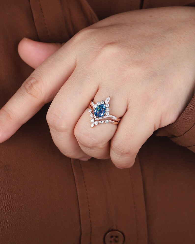 K&ouml;nnte beinhalten: Ein Verlobungsring mit einem birnenf&ouml;rmigen blauen Edelstein, einem zarten V-f&ouml;rmigen Band und kleineren wei&szlig;en Edelsteinen. Der Ring ist in Ros&eacute;gold gefasst.