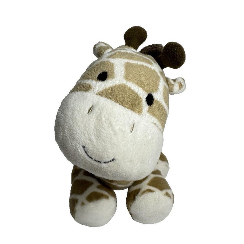 May include: A plush giraffe toy with a white face, brown eyes, and a brown nose. The giraffe is sitting with its legs tucked underneath it. The giraffe is made of soft, plush fabric and has a brown and tan patterned body.