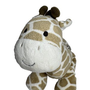 May include: A plush brown and white giraffe toy with a white face and black eyes. The giraffe is lying on its stomach with its head turned to the side. The giraffe has a brown and white patterned body.