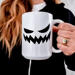 May include: White ceramic mug with a black silhouette of a grinning ghost face.