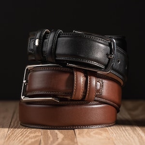 May include: Two leather belts stacked on top of each other. The top belt is black and the bottom belt is brown.