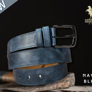 Peut inclure: Une ceinture en cuir bleu marine avec une boucle argent&eacute;e. La ceinture est enroul&eacute;e et poss&egrave;de un bord cousu. Le nom de la marque "LEGENDARY HIDE" est visible dans le coin sup&eacute;rieur droit de l'image.