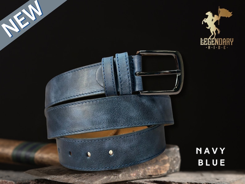 Peut inclure: Une ceinture en cuir bleu marine avec une boucle argent&eacute;e. La ceinture est enroul&eacute;e et poss&egrave;de un bord cousu. Le nom de la marque "LEGENDARY HIDE" est visible dans le coin sup&eacute;rieur droit de l'image.