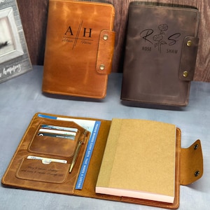 May include: Two leather-bound journals with personalized engravings. The brown journal has the initials "AH" and the name "Alan Harris". The dark brown journal has the initials "RS" and the name "Rose Shaw" with a floral design. Both journals have a pen holder and card slots.