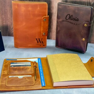 Peut inclure: Deux couvertures de journal en cuir, l'une fauve et l'autre brun fonc&eacute;, avec les initiales WA et le pr&eacute;nom Olivia. Une couverture fauve ouverte pr&eacute;sente un carnet, des fentes pour cartes, un stylo et le texte grav&eacute; Never Forget That You Are Loved.