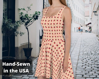 May include: A sleeveless, cream-colored dress with a strawberry print. The dress has a fitted bodice and a flared skirt. The dress is hand-sewn in the USA.