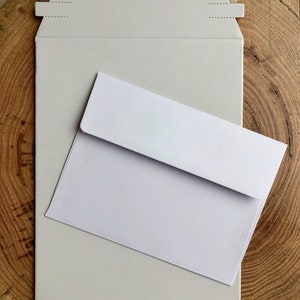 May include: A white envelope with a white mailing envelope on top of it. Both envelopes are on a wooden surface.