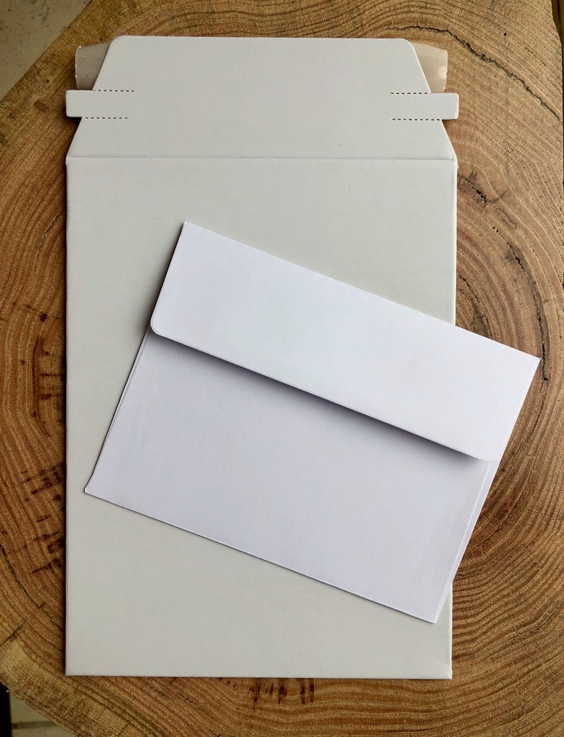 May include: A white envelope with a white mailing envelope on top of it. Both envelopes are on a wooden surface.