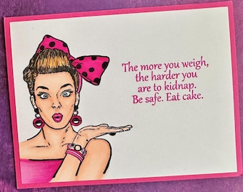 May include: A pink and white greeting card with a cartoon illustration of a woman with a pink bow in her hair. The text on the card reads: "The more you weigh, the harder you are to kidnap. Be safe. Eat cake."