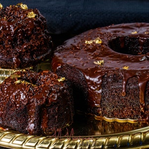 May include: Three chocolate cakes on a gold tray. The cakes are covered in chocolate icing and decorated with gold leaf.