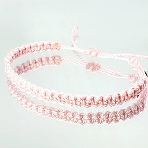 Puede incluir: Un brazalete de amistad rosa hecho de cordón trenzado con cierre anudado.