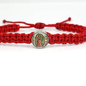 May include: Red braided string bracelet with a silver charm featuring a colorful image of the Virgin Mary.
