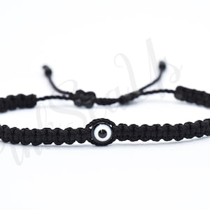 May include: Black string bracelet with a white and black evil eye charm.