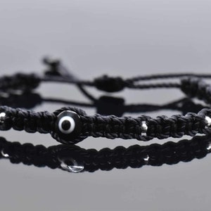 May include: Black braided bracelet with a silver bead and a black and white evil eye charm.