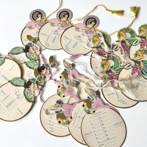 Könnte beinhalten: Eine Sammlung von Tally-Karten im Vintage-Stil mit Illustrationen von Frauen in Kleidern. Die Karten sind oval mit cremefarbenem Hintergrund und dekorativem Rand. Jede Karte hat eine Schnur und eine Quaste.