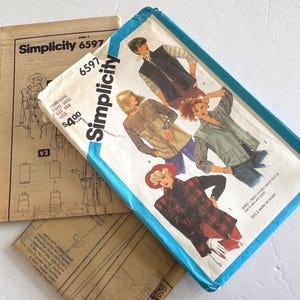 以下が含まれることがあります： ヴィンテージのSimplicityソーイングパターン。メインパターンは、ベストやジャケットなど、女性のファッションデザインのイラストを特徴としています。パターンパッケージは白地に青いトリムとSimplicityのロゴ入り。追加のパターンピースが見えます。