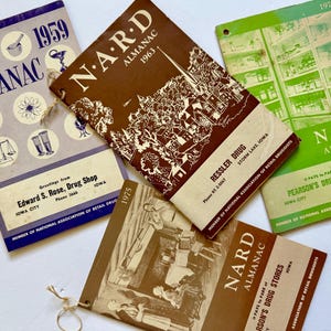 May include: Four vintage NARD Almanac booklets from 1959, 1963, 1974, and 1975. The booklets are in various colors, including blue, brown, and green. The booklets feature the names of drug stores.