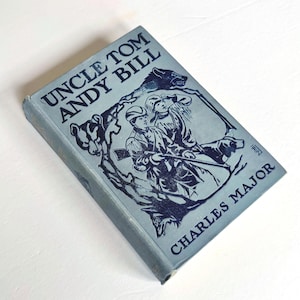May include: A vintage book titled "Uncle Tom Andy Bill" by Charles Major. The book has a light blue cover with dark blue illustrations of two men and a dog. The book is slightly worn.
