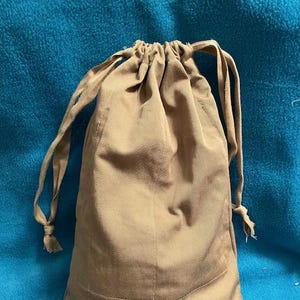 May include: A tan drawstring bag made of fabric with a gathered top and long ties.