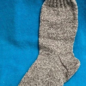 May include: A single gray wool sock, knitted with a ribbed cuff and a textured body. The sock is displayed against a solid blue background, showcasing its shape and construction. The sock appears to be a medium weight, suitable for colder weather.