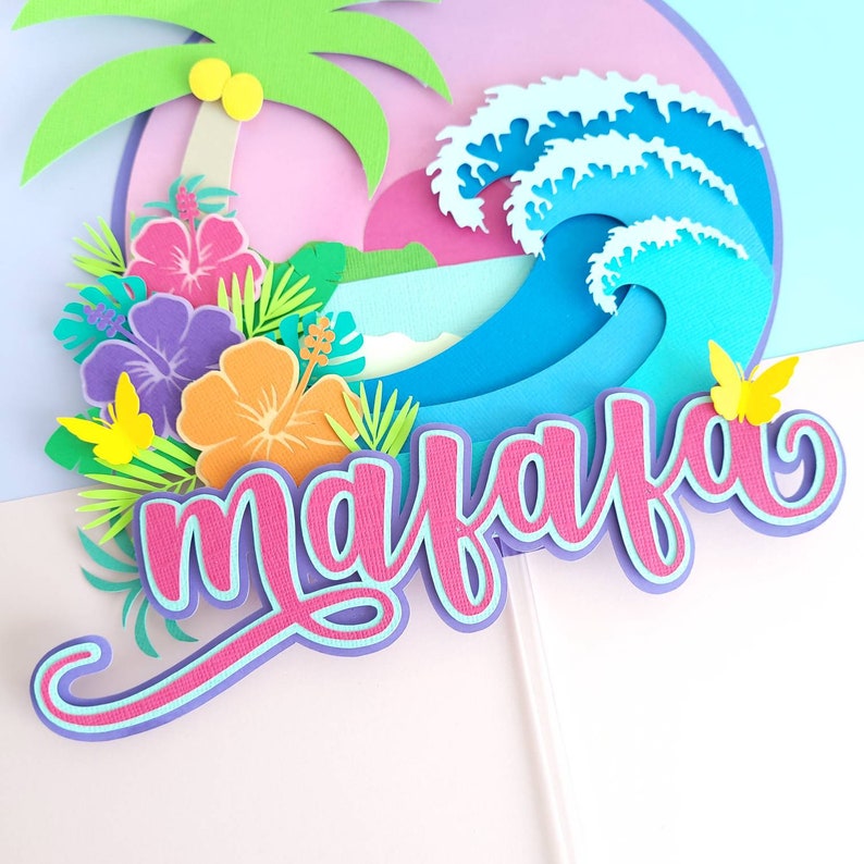 May include: A paper craft with a tropical theme. The craft features a palm tree, a wave, flowers, butterflies, and the word "mahalo" in pink and blue lettering.