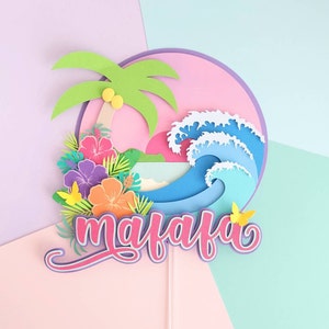 May include: A pink, blue, and green paper cake topper with a palm tree, waves, flowers, and the name "maiafa" in pink lettering.