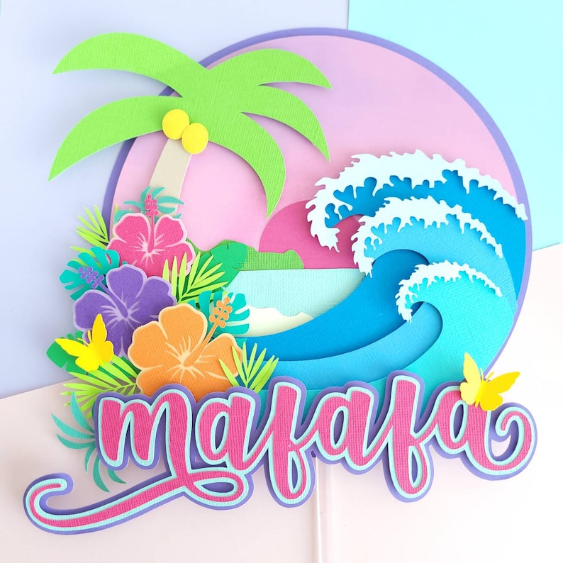 May include: A papercraft cake topper featuring a tropical theme with a palm tree, ocean waves, flowers, butterflies, and the name "maiafa" in pink and purple lettering.