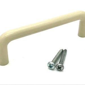 May include: A cream-coloured cabinet pull handle with a curved design, alongside two silver screws. The handle is made of a solid material and is designed for easy gripping. Suitable for furniture restoration or new builds.