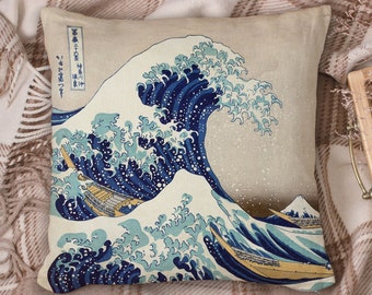 May include: A decorative pillow featuring a blue and white print of the Great Wave off Kanagawa, a famous Japanese woodblock print by Hokusai. The pillow is made of a beige fabric with a subtle texture.