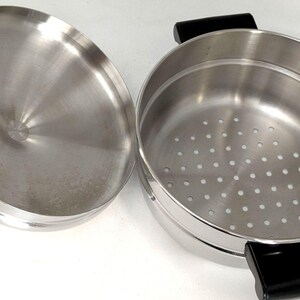以下が含まれることがあります： ステンレス製の蒸し器と蓋のセット。鍋の底には蒸し料理用の穴が開いており、両サイドには黒い耐熱プラスチック製の取っ手がついています。鍋の内側と蓋の裏側はメタリックシルバー色です。