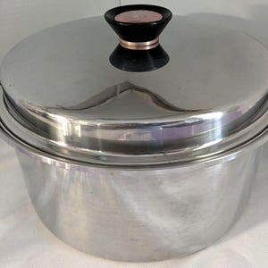 以下が含まれることがあります： ステンレス製の調理鍋と蓋。鍋には2つの黒いハンドルと、蓋には黒とローズゴールドのノブが付いています。鍋は光沢のある、つや消し金属で作られています。