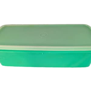 May include: A rectangular, green plastic container with a matching lid. The lid is a lighter shade of green and has a circular indentation in the center. The container is likely used for food storage.
