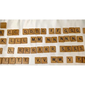 May include: A set of wooden Scrabble tiles with letters and point values. The tiles are arranged in rows, with the letters B, C, D, F, G, H, J, K, L, M, N, P, Q, R, S, T, V, W, X, Y, and Z.