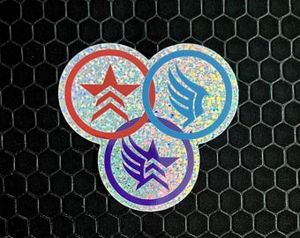 May include: Three iridescent glitter stickers with different designs. The first sticker is red with a white star and a white chevron. The second sticker is blue with a white wing. The third sticker is purple with a white wing and a white star.