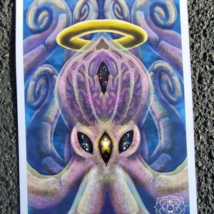 Puede incluir: Una ilustración psicodélica de una criatura de múltiples ojos y tentáculos con un halo sobre su cabeza. La criatura está representada en tonos de púrpura, rosa y azul sobre un fondo azul. La imagen está firmada "DECAF" en la esquina inferior derecha.