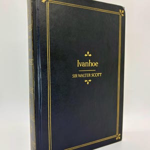 May include: A hardcover book titled "Ivanhoe" by Sir Walter Scott. The book has a dark blue cover with gold lettering and decorative gold borders. The spine is also dark blue with gold accents. The book is in good condition.