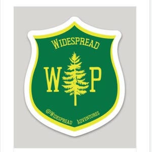 May include: A green and yellow shield-shaped sticker with the text "WIDESPREAD" at the top, "WP" in large letters in the center, and a yellow pine tree between the letters. The text "@WIDESPREAD ADVENTURES" is at the bottom.