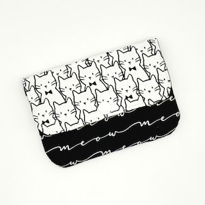May include: A black and white clutch featuring a repeating pattern of cartoon cats with bow ties. The bottom section is black with the word "meow" in a white, cursive font. The clutch is closed with a white button.