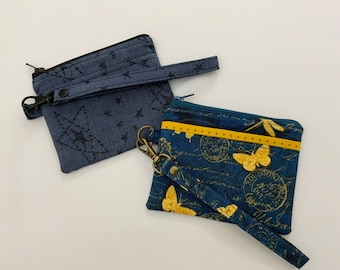 May include: Two small zippered pouches with wrist straps. One pouch is blue with a star pattern and the other is blue with a yellow butterfly and dragonfly pattern.