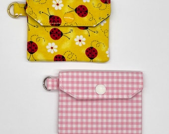 May include: Two fabric pouches with snap closures. The first pouch is yellow with a ladybug print and a white daisy print. The second pouch is pink with a white gingham pattern.