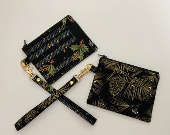 May include: Two small zippered pouches with black fabric and gold accents. One pouch has a musical note and holly leaf pattern. The other pouch has a pine cone and pine needle pattern. A black and gold strap with a gold clasp connects the two pouches.